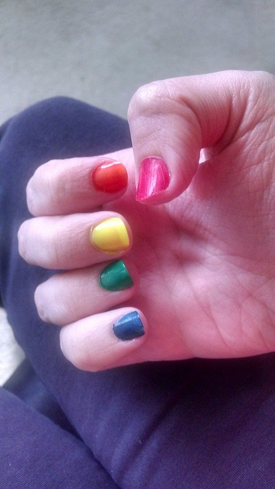 Photo of a hand with painted nails. Each nail is a different color of the rainbow with the thumb being red and pinky being blue.